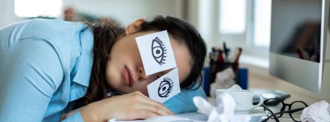 Les Français ne dorment pas suffisamment ce qui a impact sur leur travail Femme dormant sur son bureau de travail, avec des post-it imitant les yeux ouverts