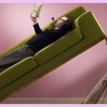 Un homme allongé sur un canapé et sa femme qui passe l'aspirateur