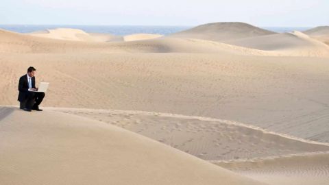 Homme seul au milei d'un désert travaillant sur son ordinateur en costume