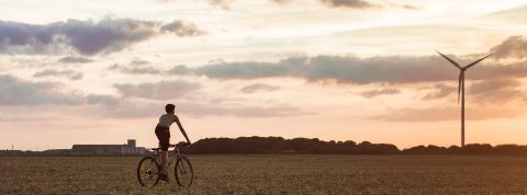 Tout savoir sur le bilan carbone pour les entreprises Jeune garçon sur son vélo se dirigeant vers une éolienne en fin de journée