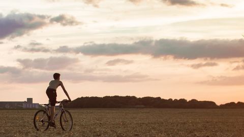 Jeune garçon sur son vélo se dirigeant vers une éolienne en fin de journée