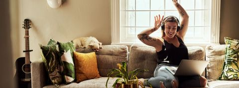 Si le temps passé en ligne est en baisse (- 5 % en un an), l'usage des réseaux sociaux a quant à lui augmenté. Femme sur son canapé, un casque sur les oreilles et un oridnateur sur les genoux, levant les bras