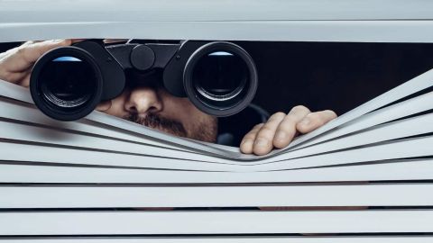 96 % des entreprises surveillent leurs employés au travail Personne derrière une persienne avec des jumelles