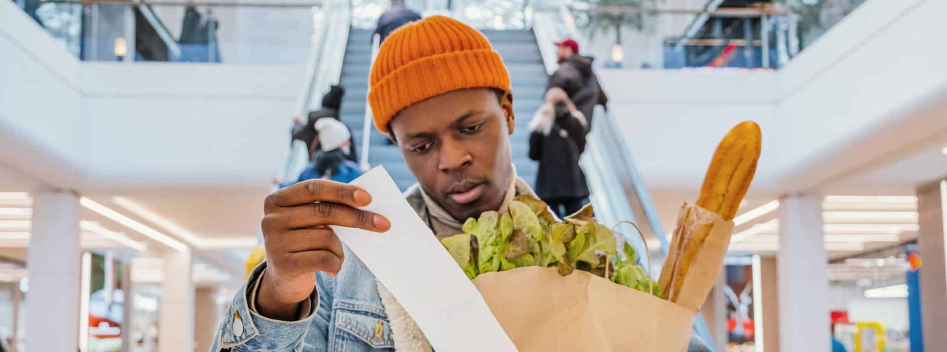 la nouvelle équation du « bien manger » est menacée par l’inflation, contraignant les Français à faire des compromis. - L'ADN Homme portant des courses et regardant son ticket de caisse