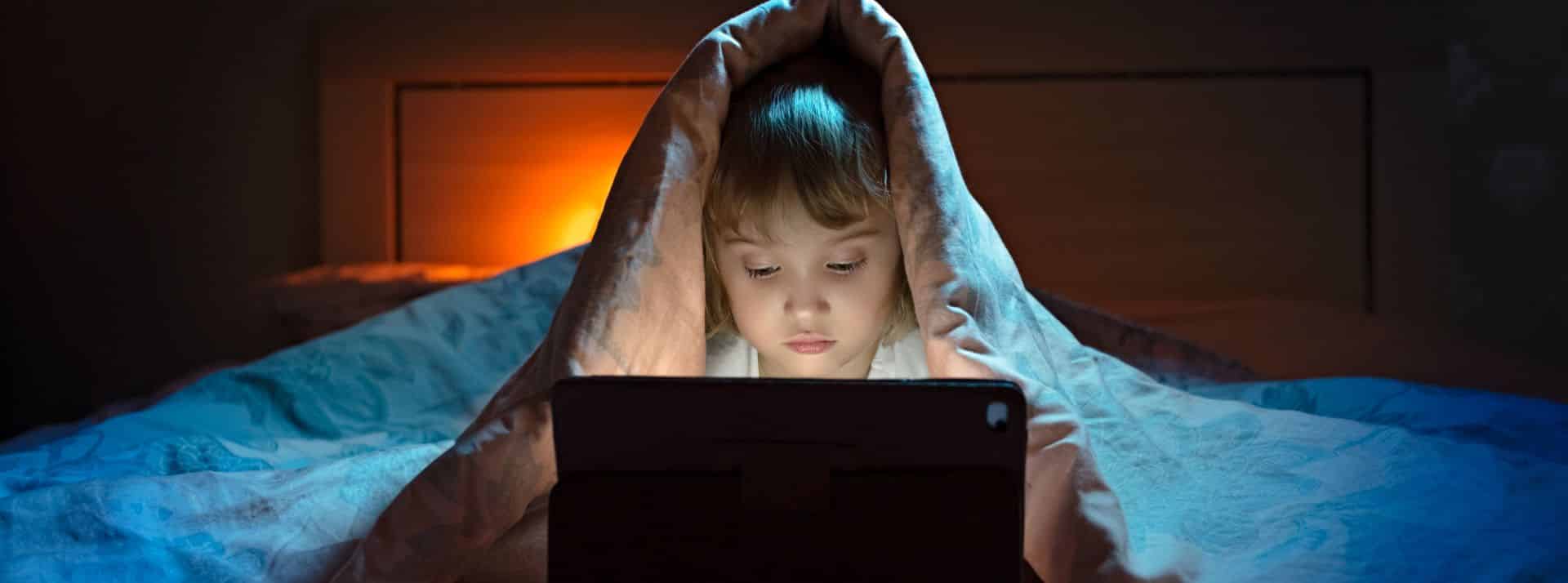 Jeune enfant sous sa couette avec un ordinateur