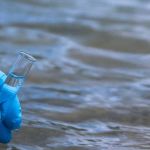 La main d’un homme dans un gant bleu prend un gros plan d’eau dans un tube à essai pour mesurer la pollution de l’eau