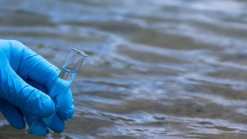 La main d’un homme dans un gant bleu prend un gros plan d’eau dans un tube à essai pour mesurer la pollution de l’eau