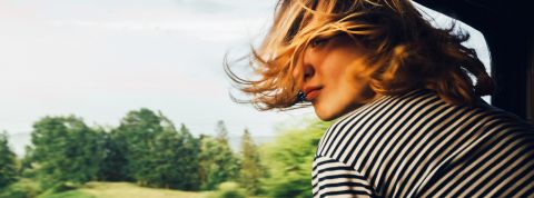 Tendance mobilités : ceux qui aiment la planète prendront le train... s'il y en a ! Femme cheveux au vent à la fenêtre d'un train