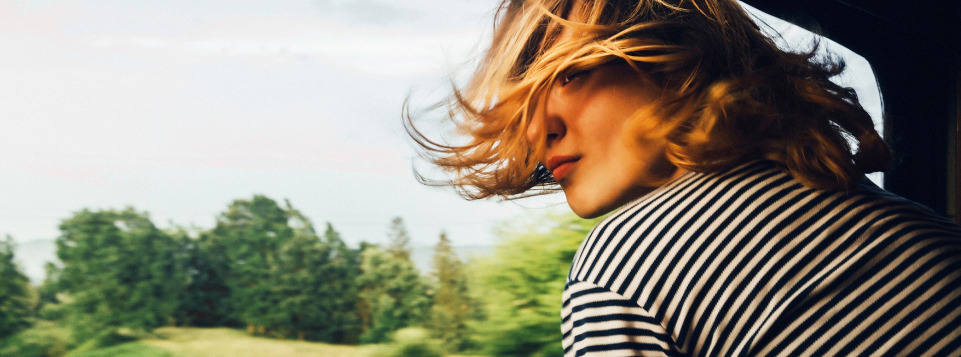 Tendance mobilités : ceux qui aiment la planète prendront le train... s'il y en a ! Femme cheveux au vent à la fenêtre d'un train