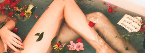 Cosmétiques bio et naturel s'imposent comme des incontournables dans les salles de bains. Jambe d'une femme dans une baignore avec des pétales de fleurs