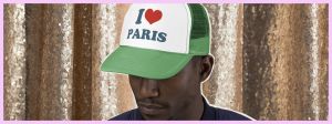 Homme noir portant une casquette I love Paris sur un rideau pailleté