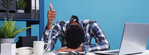 Les Francais sont parmi les travailleurs les moins engagés d'Europe. homme la tête posée sur son bureau, un pouce en l'air