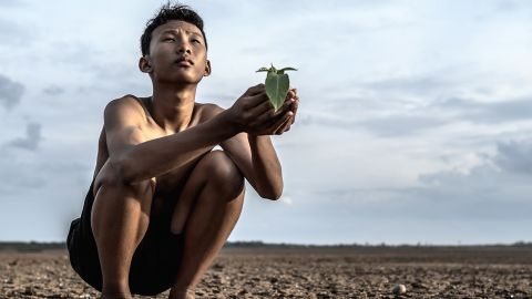Jeune homme asiatique accroupi sur une terre craquelee regarde le ciel