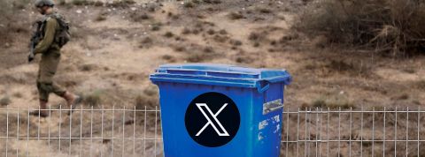 En laissant courir la désinformation, Elon Musk est-il complice des terroristes ? Poubelle bleue avec logo X, devant barrière et soldat en fond