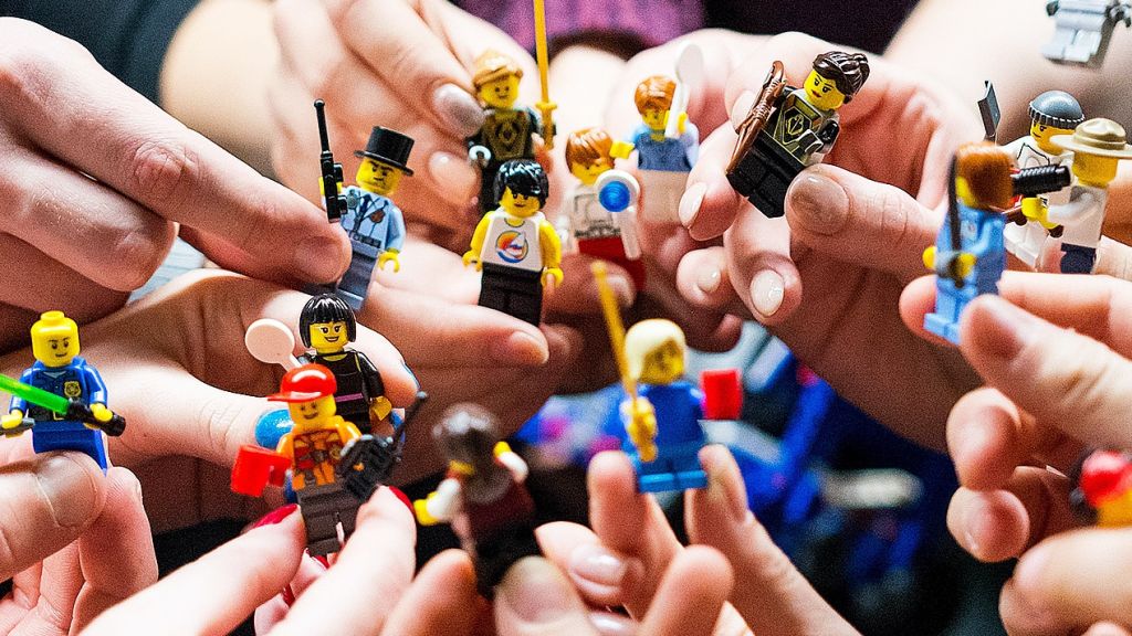 Des mains adultes tiennent des mini personnages LEGO, comme une équipe