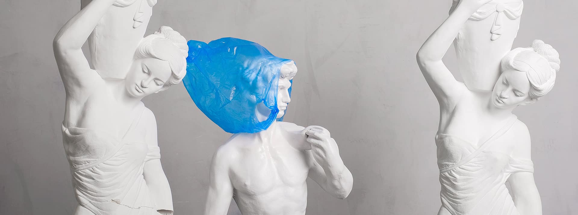 La pollution plastique : une urgence à ne pas confier à une IA - L'ADN Des statues dont l'une avec un sac plastique bleu sur la tête
