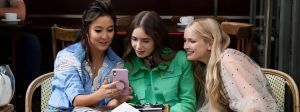 Emily in Paris et ses deux amies regardent un téléphone à la terrasse d'un café