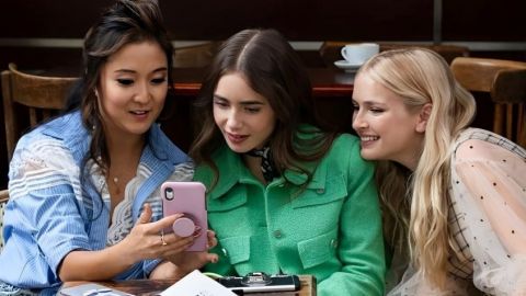 Emily in Paris et ses deux amies regardent un téléphone à la terrasse d'un café