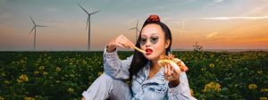 Montage d'une fille asiatiquequi mange un hot dog devant un champ de fleurs avec des éoliennes au fond