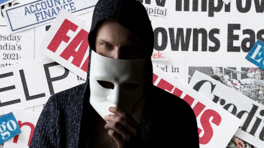 Homme avec un masque anonymous devant des coupures de journaux