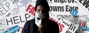 Homme avec un masque anonymous devant des coupures de journaux