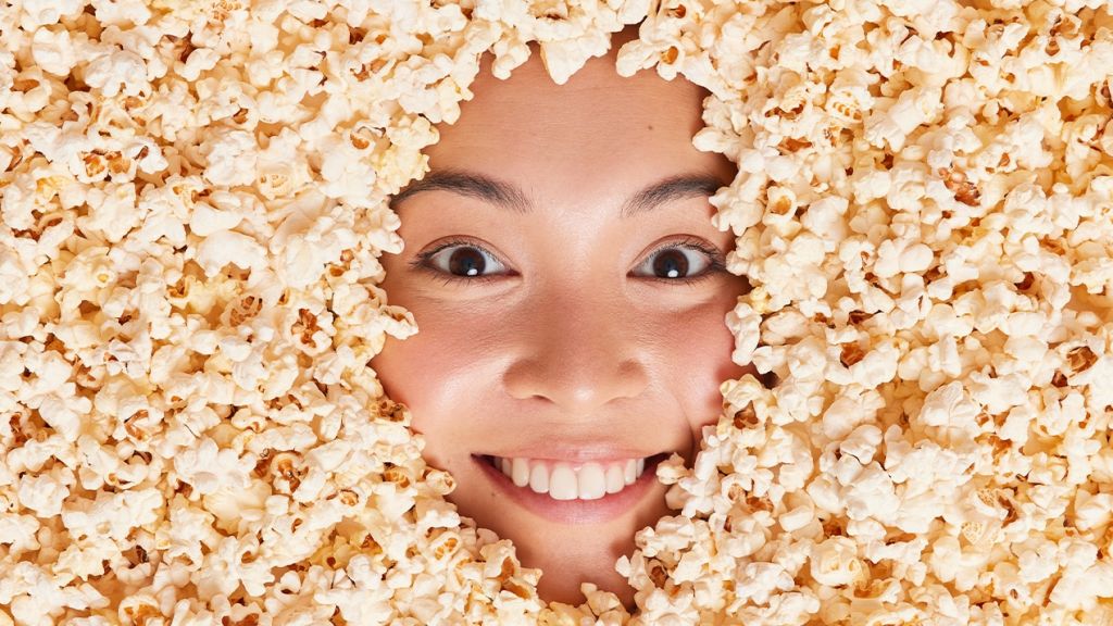 Comment Big Food exploite la tendance Anti-Diet pour protéger ses intérêts Le visage d'une jeune Asiatique ensevelie sous des pop corn
