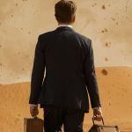 Un homme en costume de dos avec sa valise dans un désert agité