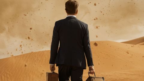 Un homme en costume de dos avec sa valise dans un désert agité