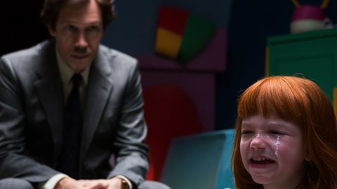 Un petite fille pleure avec un homme au second plan, dans la pénombre