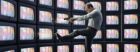 Les médias qui signent des accords avec OpenAI se tirent-ils une balle dans le pied ? Illustration d'un homme qui se tire une balle dans le pied devant un mur d'écrans de TV