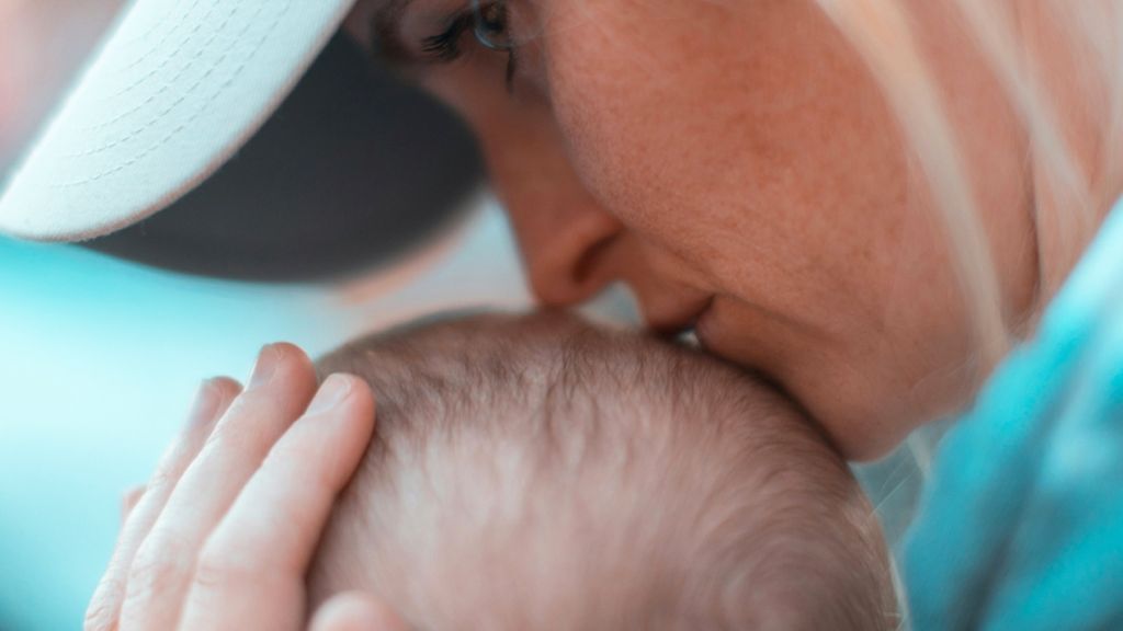 Une maman de profil embrasse le crâne de son bébé, regard dans le vague
