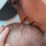 Une maman de profil embrasse le crâne de son bébé, regard dans le vague