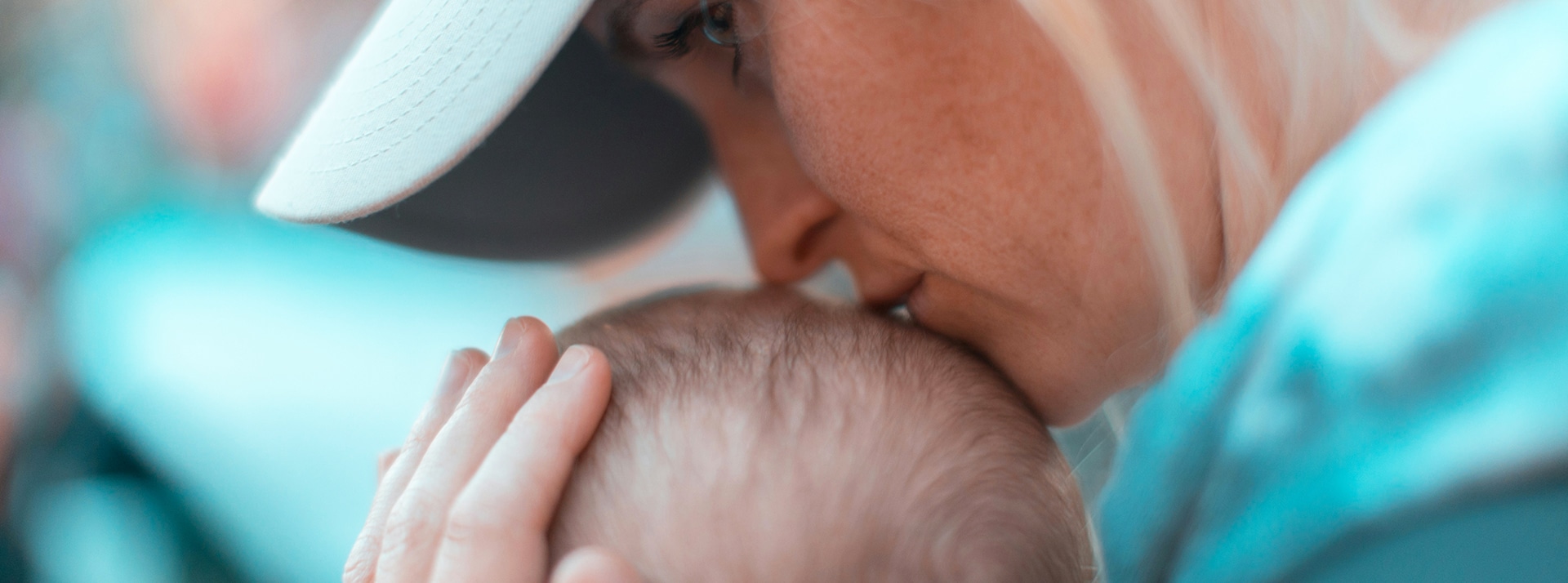 Une maman de profil embrasse le crâne de son bébé, regard dans le vague