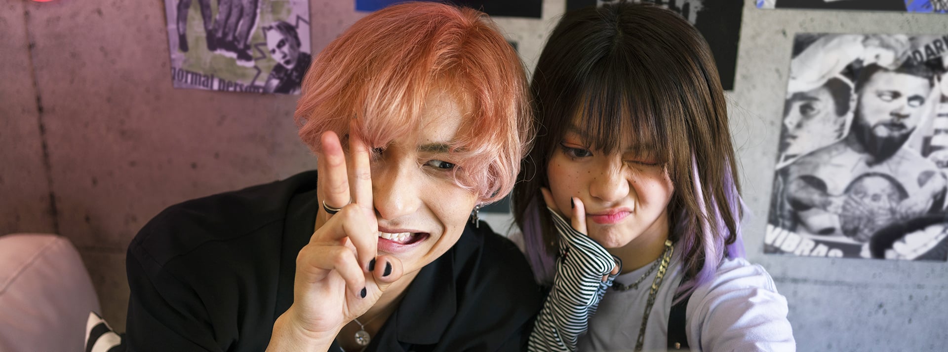 Un jeune homme cheveux orange et une jeune fille brune, tous deux asiatiques font des grimaces