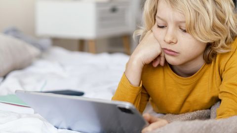 Un jeune garçon blond sur son lit avec un Ipad