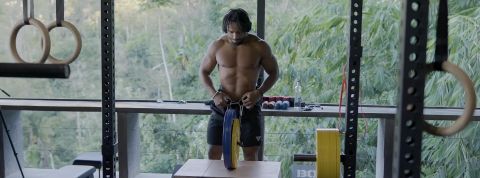 Au Bali Time Chamber, on veut « bâtir la prochaine génération d’hommes forts » Un homme métissé fait de la musculation avec en fond la jungle de Bali