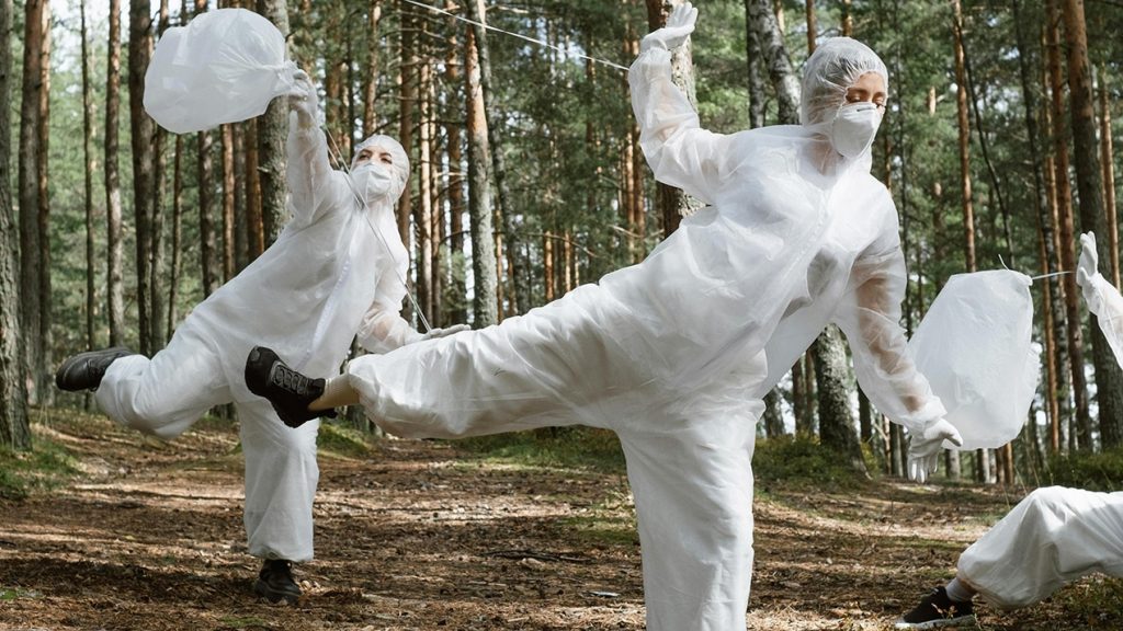 3 personnes en forêt dansent en combinaisons blanches en ramassant des déchets