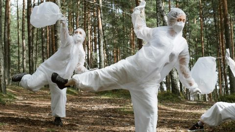 3 personnes en forêt dansent en combinaisons blanches en ramassant des déchets
