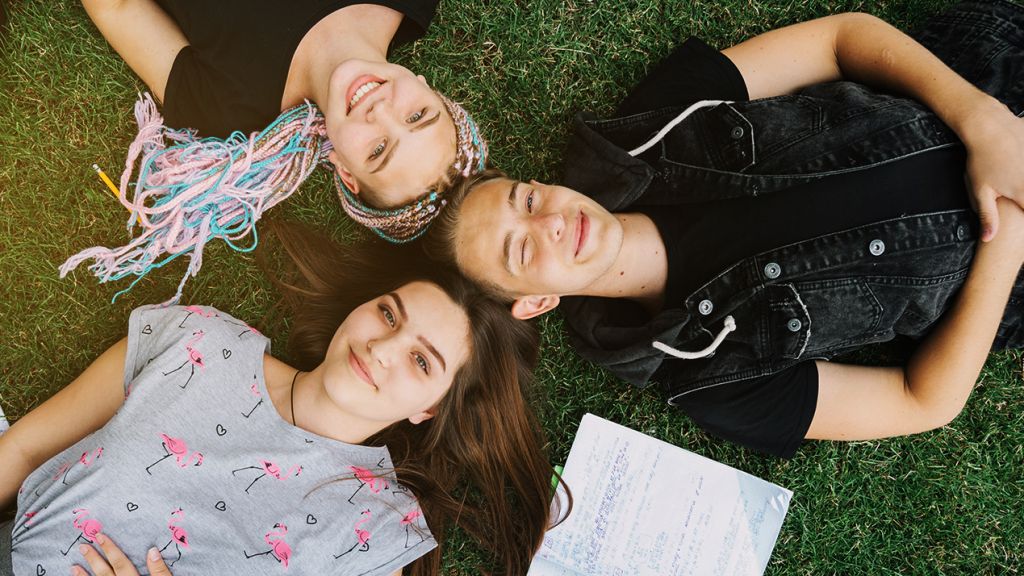 Pour former nos enfants à la crise du climat, on a trouvé une solution simple et réjouissante Des adolescents joyeux allongés sur l'herbe avec leurs cahiers ouverts