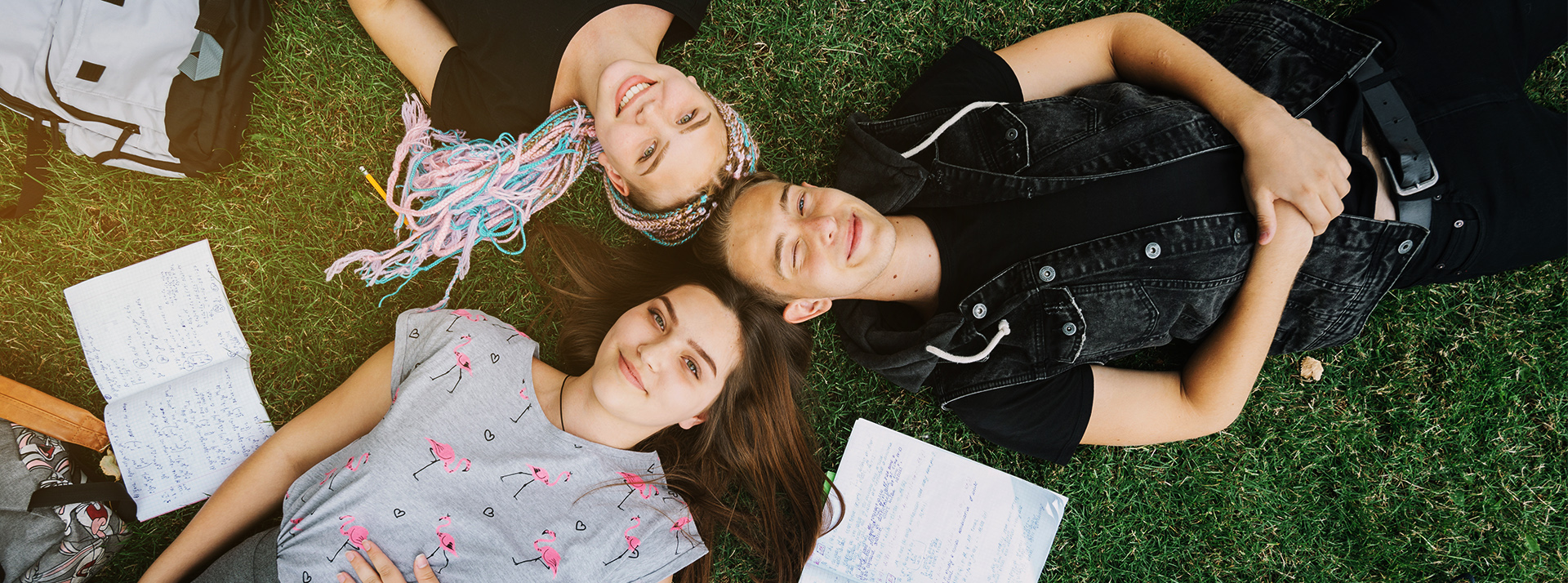 Des adolescents joyeux allongés sur l'herbe avec leurs cahiers ouverts