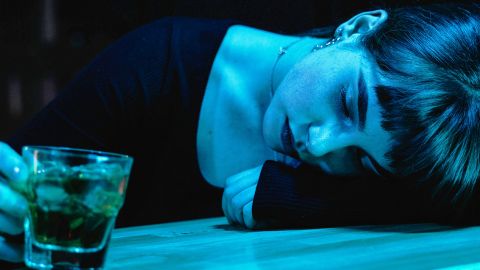 Une jeune femme avec un verra à la main effondrée sur un bar