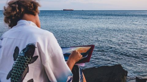 Un jeune homme de dos peint la mer