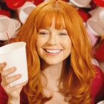 Une jolie femme rousse entourée de gobelets en plastique de couleurs