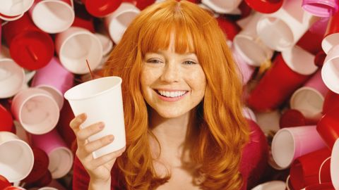 Une jolie femme rousse entourée de gobelets en plastique de couleurs