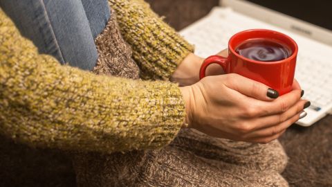 Une femme avec gros pulle et grosses chaussettes tient un mug de thé brûlant pour se réchauffer