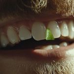 Le sourire d'un homme barbu avec un bout de salade coincé entre les dents