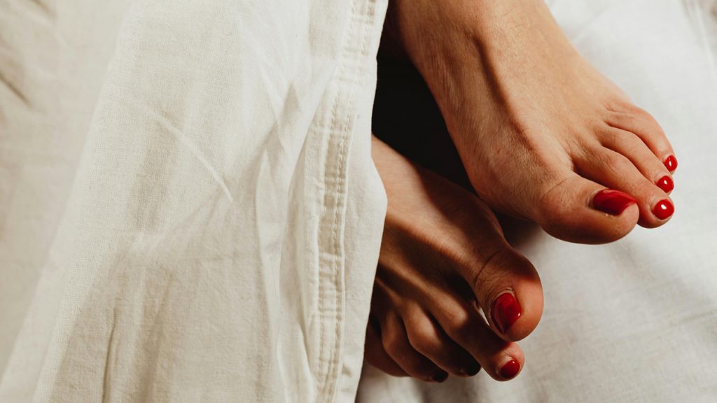 Une paire de pieds féminins avec vernis rouge dépasse d'une couette