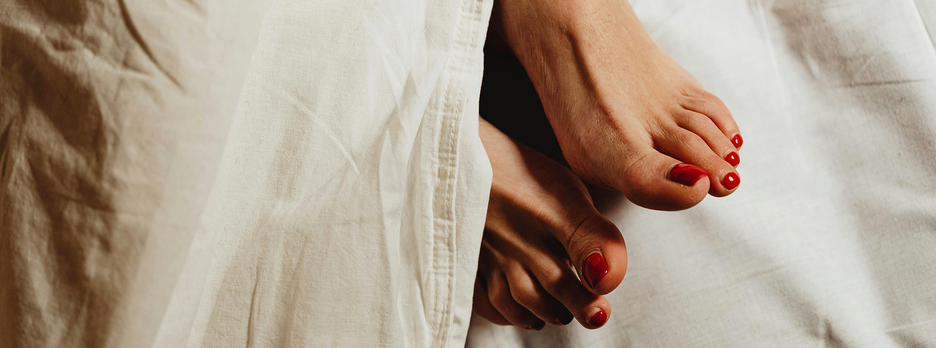Une paire de pieds féminins avec vernis rouge dépasse d'une couette