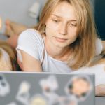 Une jeune femme sur son lit devant son ordi avec ses deux chiens