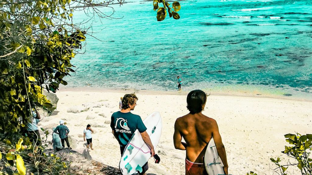 « Je pars à Bali en octobre, qui est partant ? » : Le covoyage séduit une génération en quête de liberté Deux surfers et plusierus personnes sur une plage balinaise